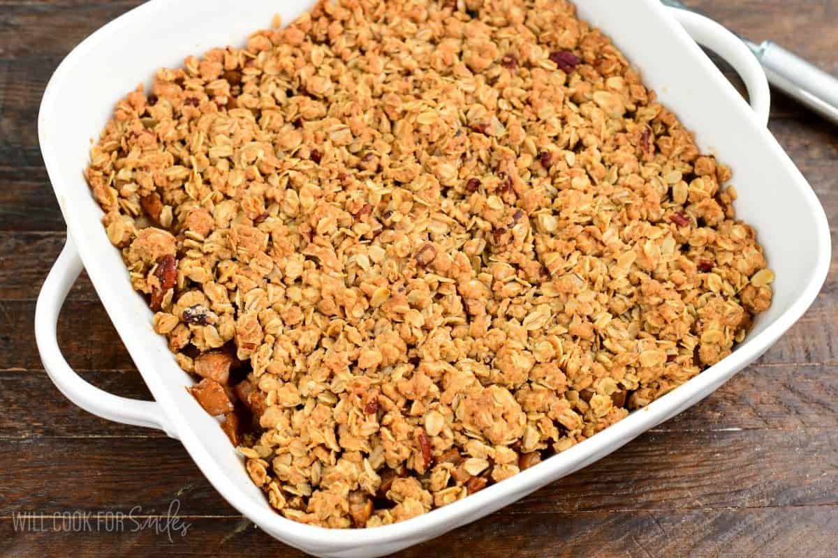 Freshly baked pear crisp with a golden oat and pecan crumble topping in a white baking dish.