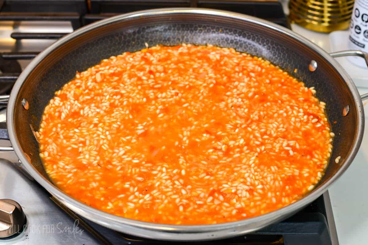 tomato risotto cooking in a large cooking pan with veggies and broth,