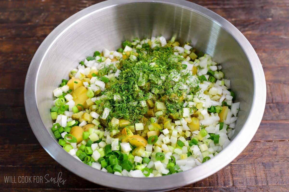 Potatoes, pickles, onions, green onions, and fresh dill combined in a mixing bowl before adding dressing.