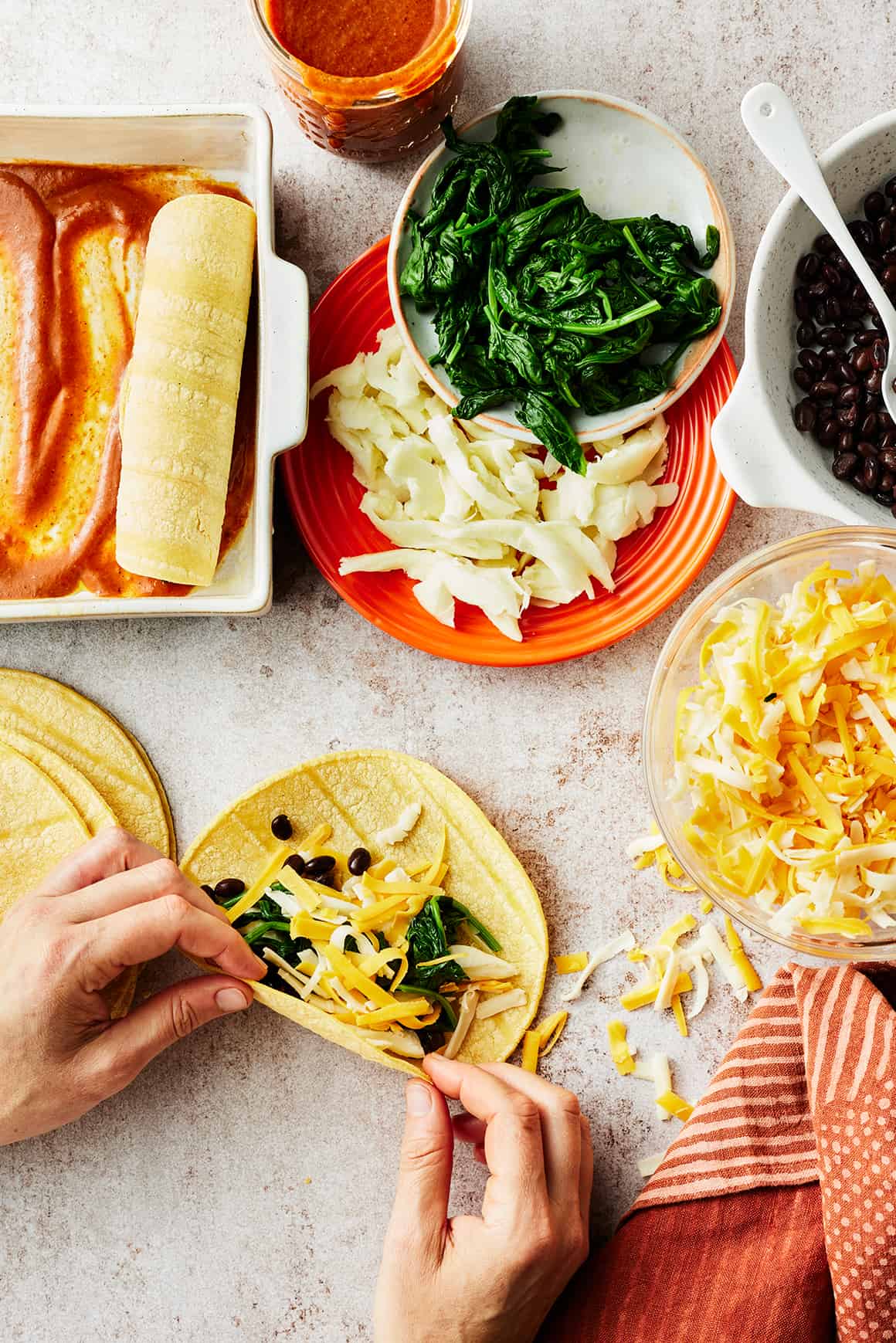 Hand rolling shredded cheese, black beans, and spinach in a corn tortilla
