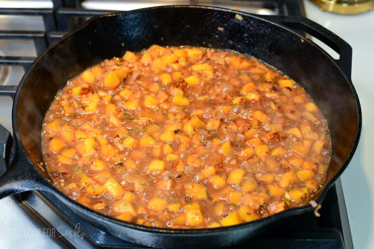 Peach sauce simmering in a cast-iron skillet, with diced peaches and onions reduced into a savory glaze.