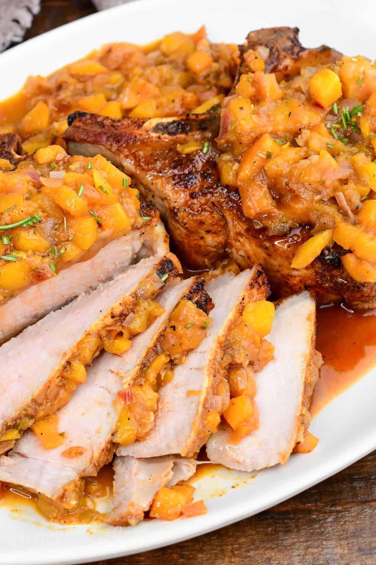 Sliced peach pork chops topped with chunky peach sauce, served on a platter with sweet and savory pan juices.