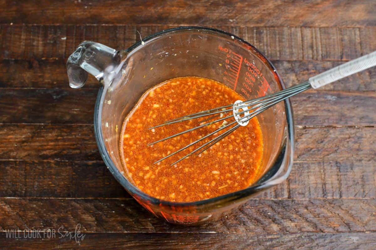 Sweet and spicy stir-fry sauce whisked together in a measuring cup with garlic and seasonings.