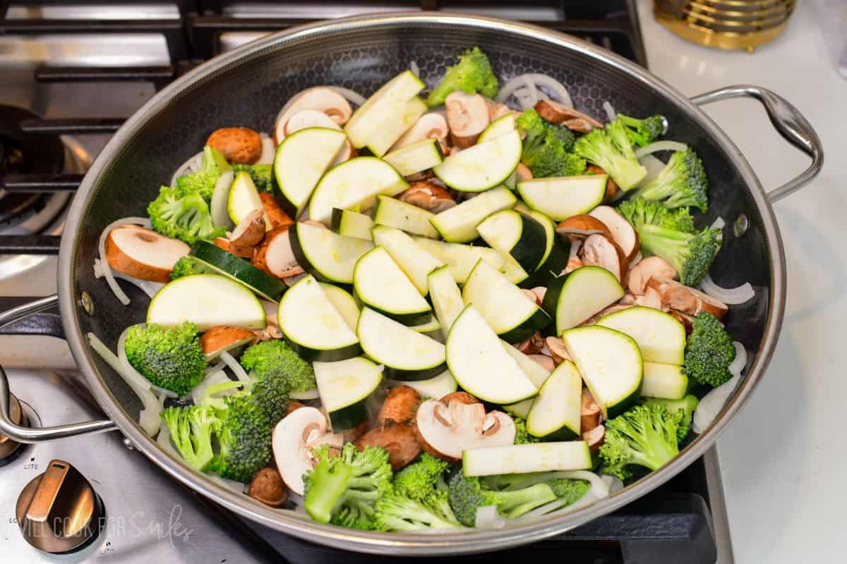Broccoli, mushrooms, onion, and zucchini cooking together in a large skillet for vegetable stir-fry.
