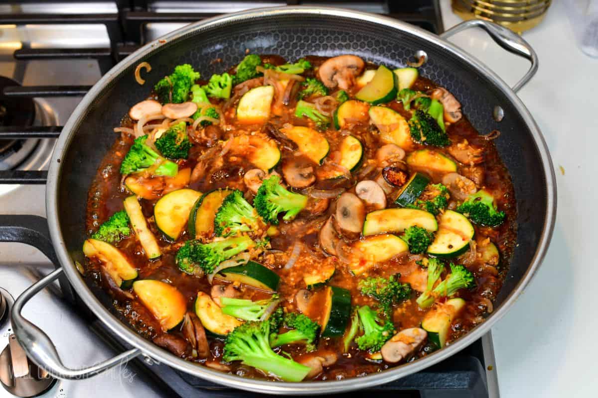 Zucchini, broccoli, mushrooms, and onions simmering in a savory stir-fry sauce in a large skillet.
